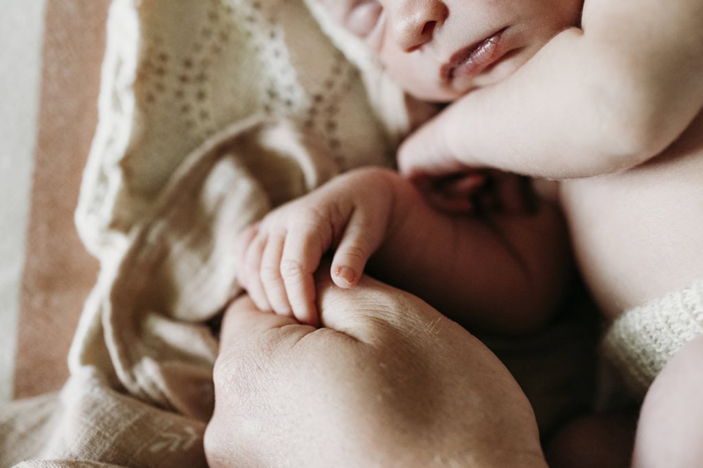 A newborn baby holds onto her father's hand.