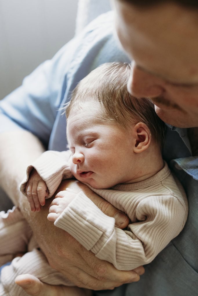 A father holds his newborn baby against his chest as light illuminates them from the window.
