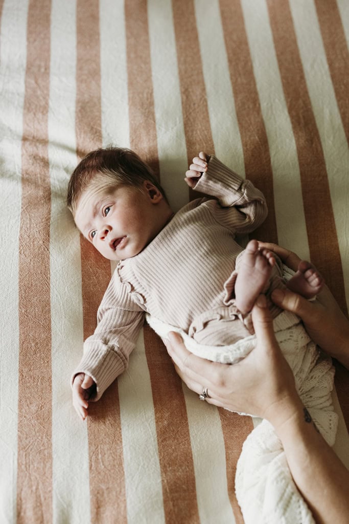 A newborn baby looks out a window as she lies on a bed in her home.