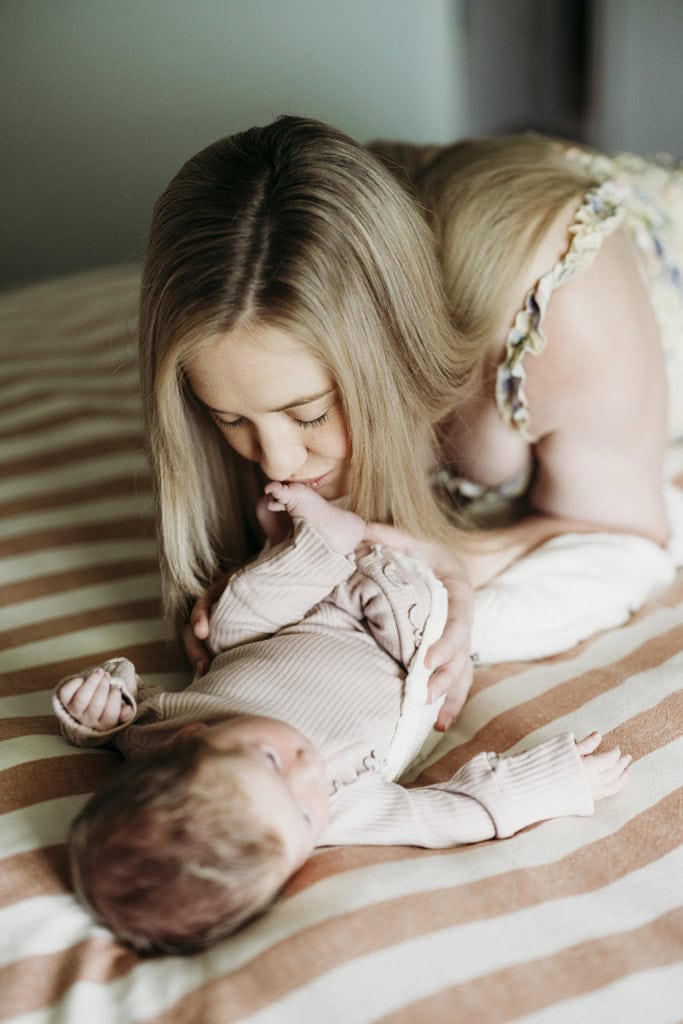 A mother gently kisses her newborn baby's foot as she lies down in their home at Rockhampton.