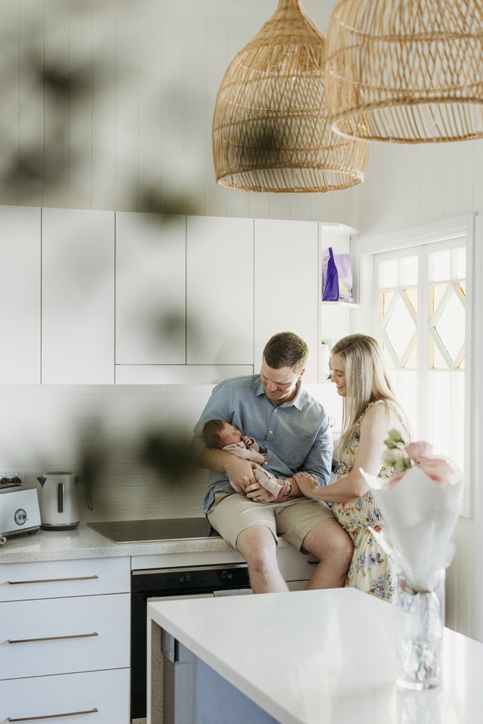 Parents hold their newborn baby in their arms as they stand in their kitchen at their home.