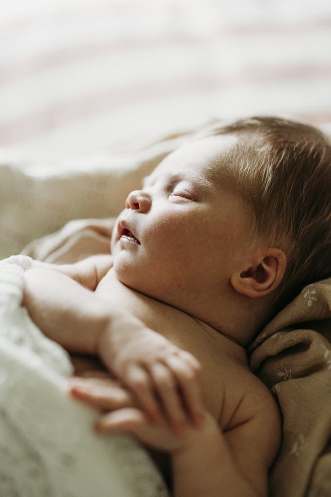 A newborn baby lays asleep as she has her hands on her chest.