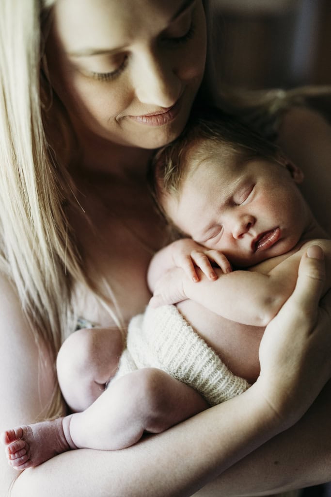 A mother cradles her newborn against her chest as she smiles.