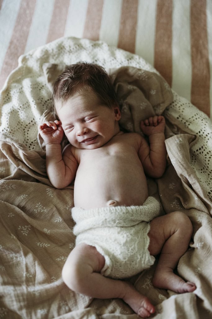 A newborn baby lays asleep on a blanket as she smiles.