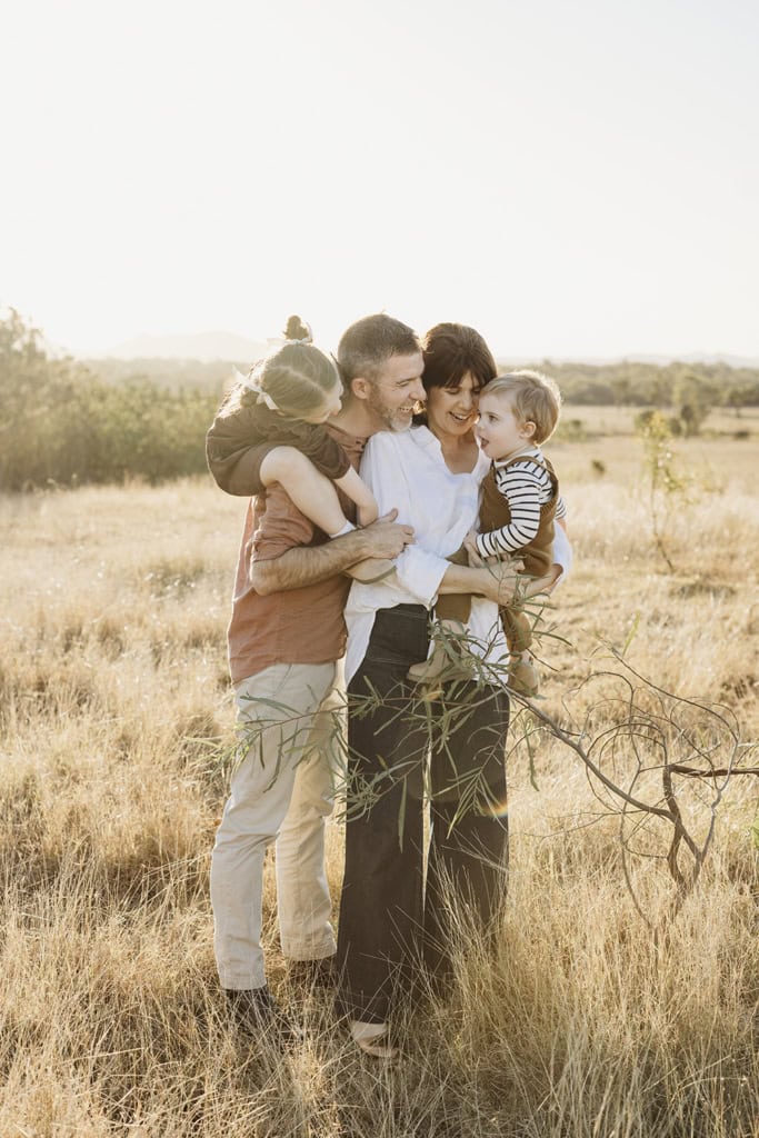 A family of four cuddle with each other as the sun sets behind them.