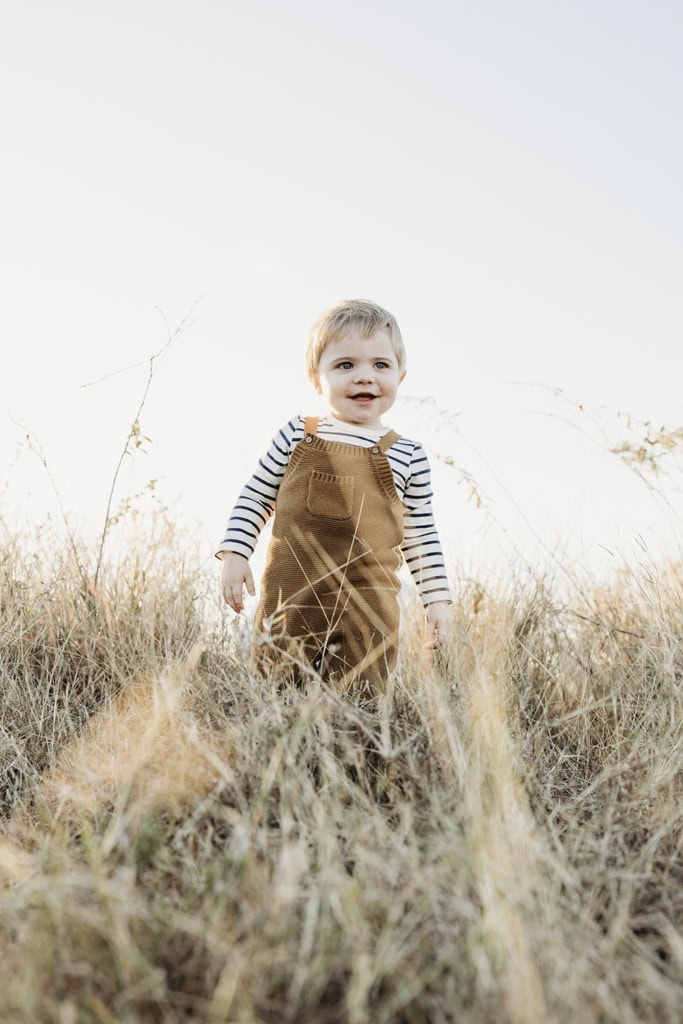 A toddler plays in long grass and laughs.