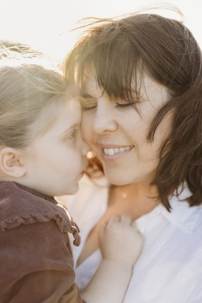 A child presses her face into her mother's cheek as her mother smiles.