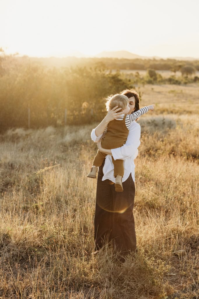 A mother cradles her toddler lovingly as the sun sets behind them.