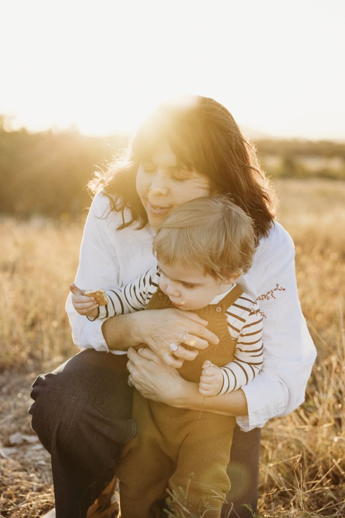 A mother cuddles her toddler as the sun sets behind them.