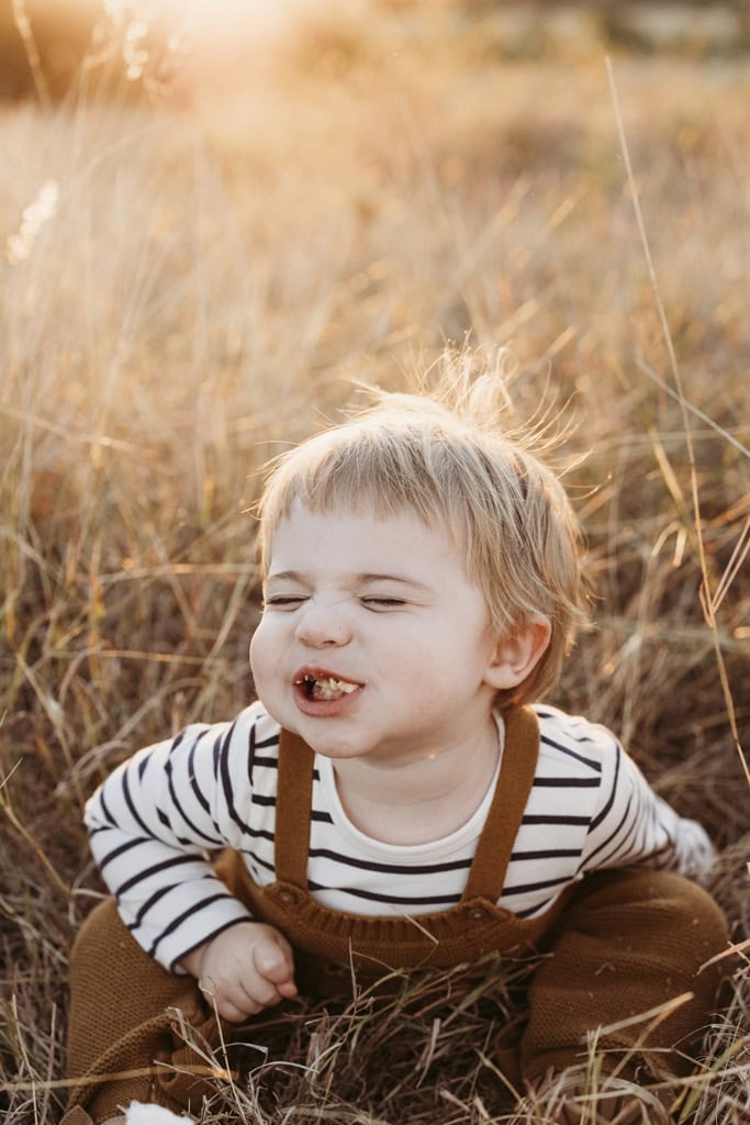 A toddler's mouth is full of food as he smiles cheekily.