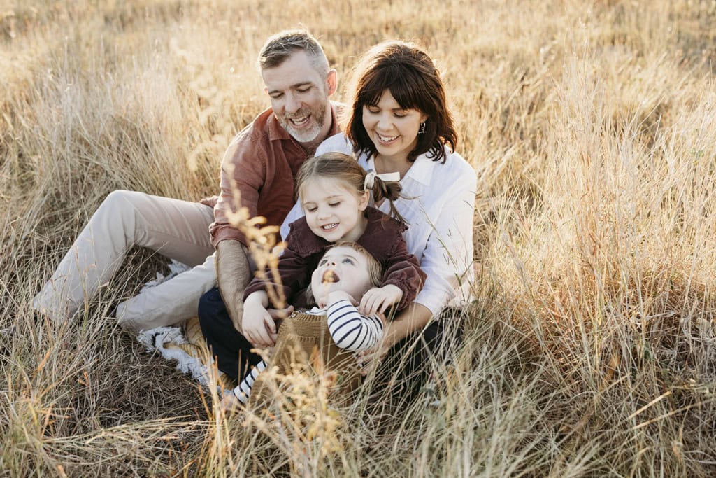 A family of four giggle as they sit together in a paddock.