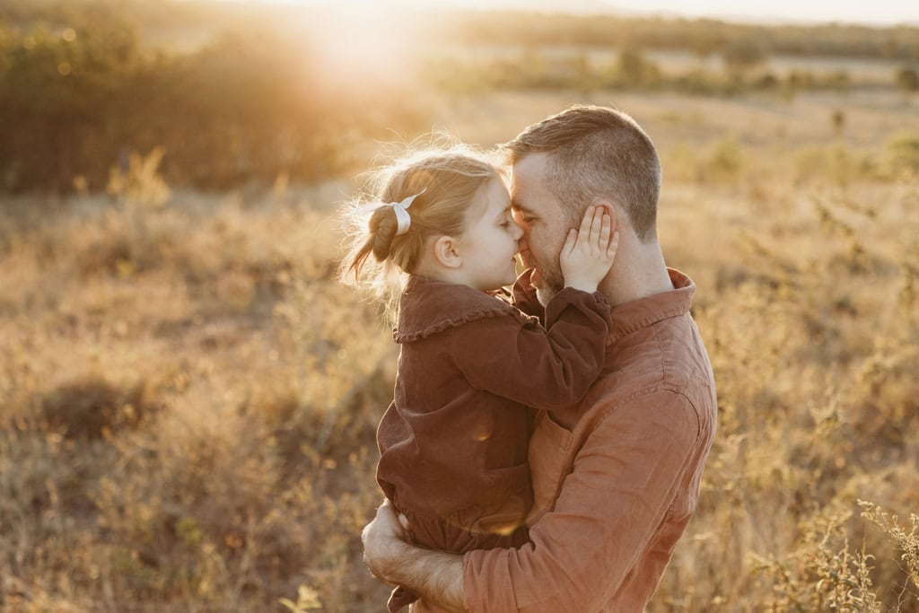 A little girl holds her father's face as they press their faces together.