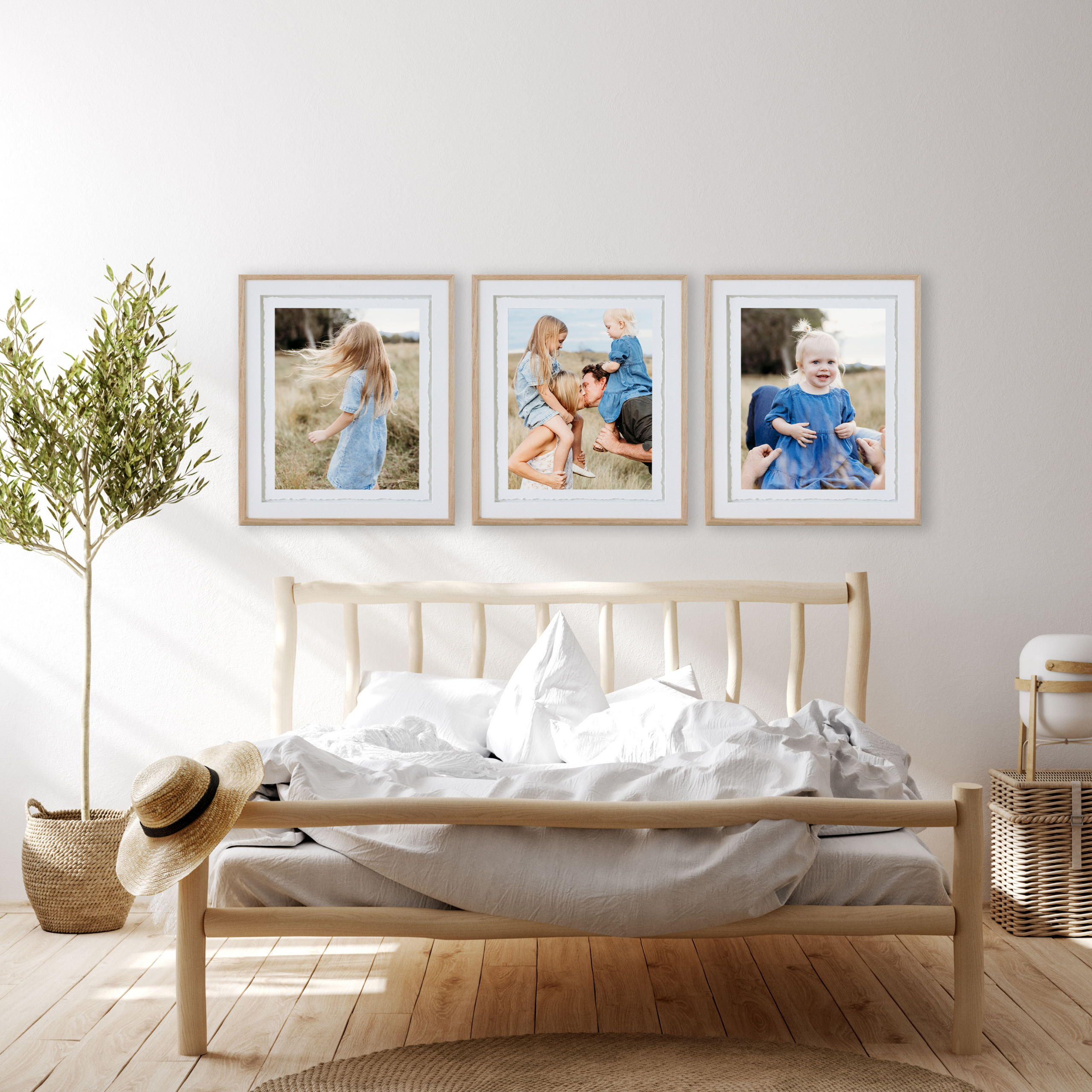 A collection of three frames with family portraits hangs above a timber bed, as light streams through the window.