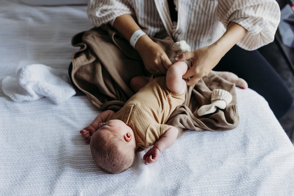 A mother dresses her newborn baby as he lies on a hospital bed.
