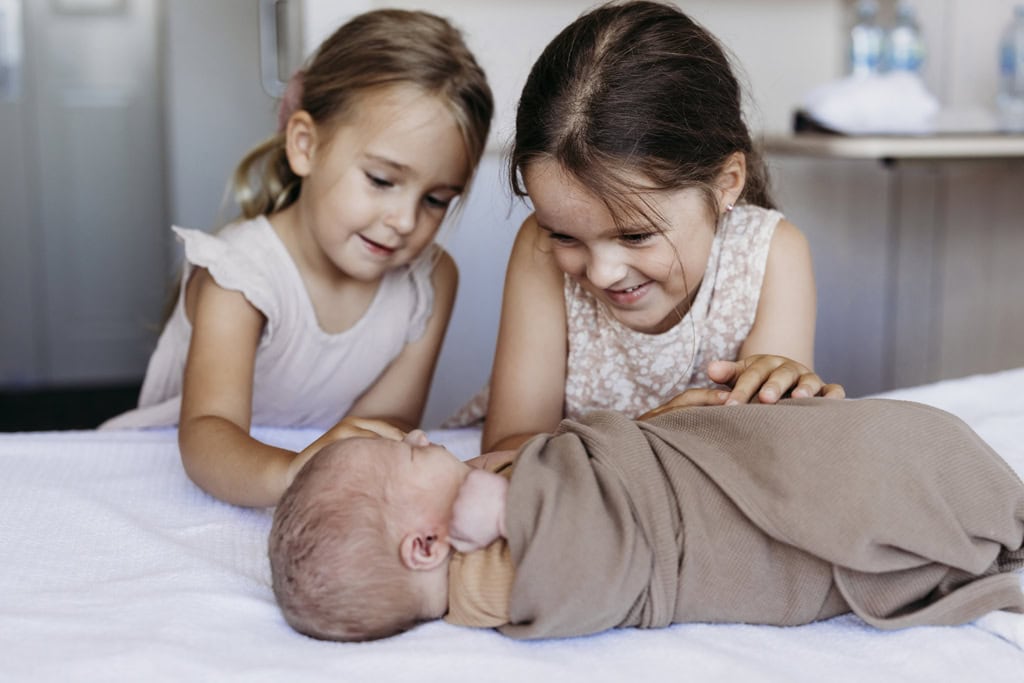 Two children look lovingly at their newborn baby brother as he lies on a hospital bed at the Mater Rockhampton.