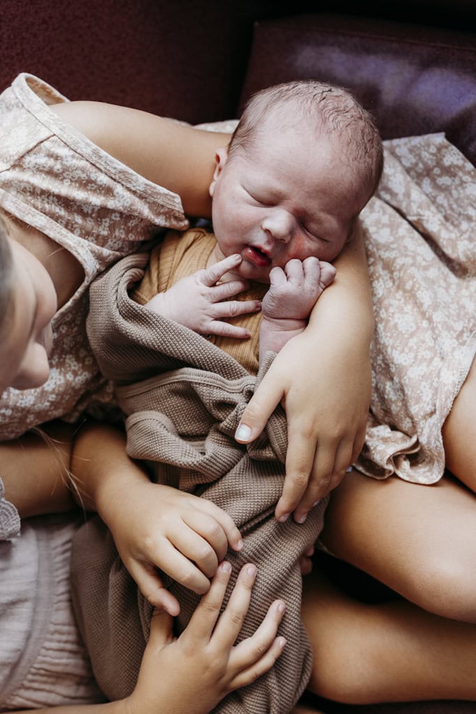 A newborn baby is held by his siblings in hospital.