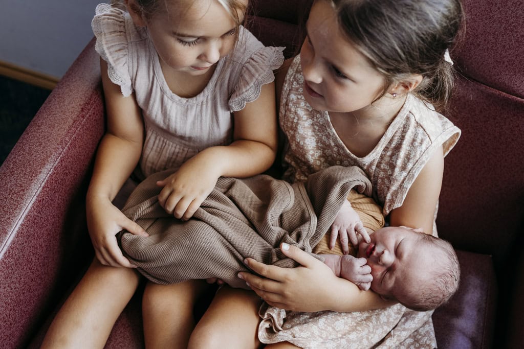 Two children hold their newborn sibling for the first time. 