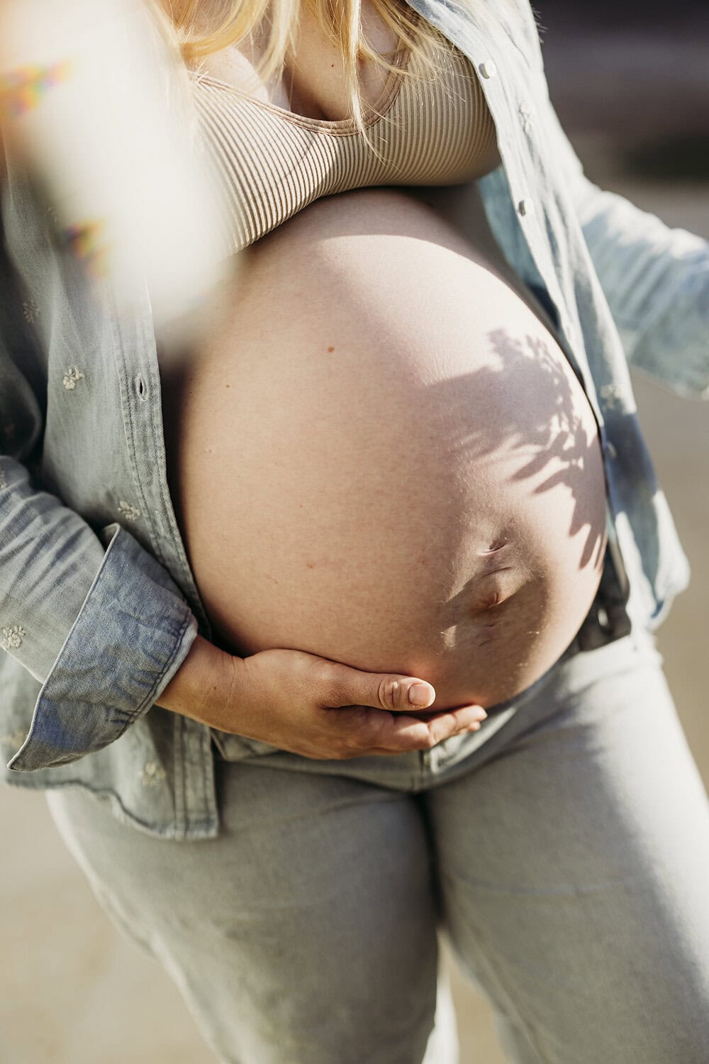A pregnant woman's belly is illuminated by morning sunlight.